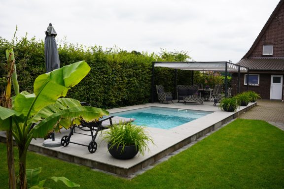 Gartenbereich mit Pool, Liegen, Sonnenschirm und grünen Pflanzen.