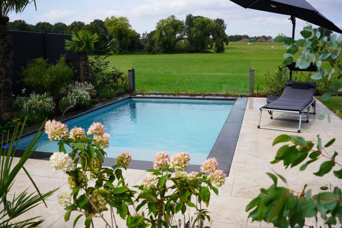 Ein klarer Pool umgeben von Pflanzen und einem Liegestuhl in einer grünen Landschaft.