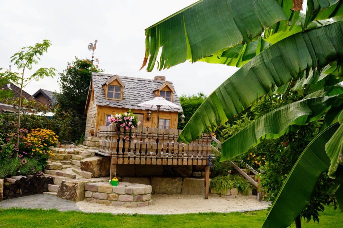 Schmuckes Holzhaus mit Balkon, umgeben von Pflanzen und einer grünen Terrasse.