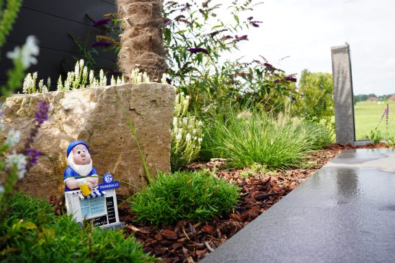 Bunte Gartendekoration mit Zwergfigur, Steinen und grünen Pflanzen.