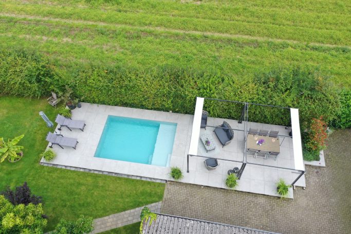 Poolanlage mit Rasen, Liegen und überdachtem Sitzbereich.