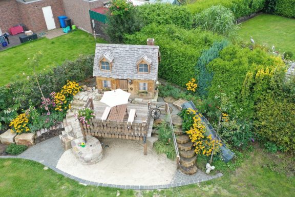 Ein kleines, charmantes Haus mit Garten und bepflanzten Beeten in einer grünen Umgebung.
