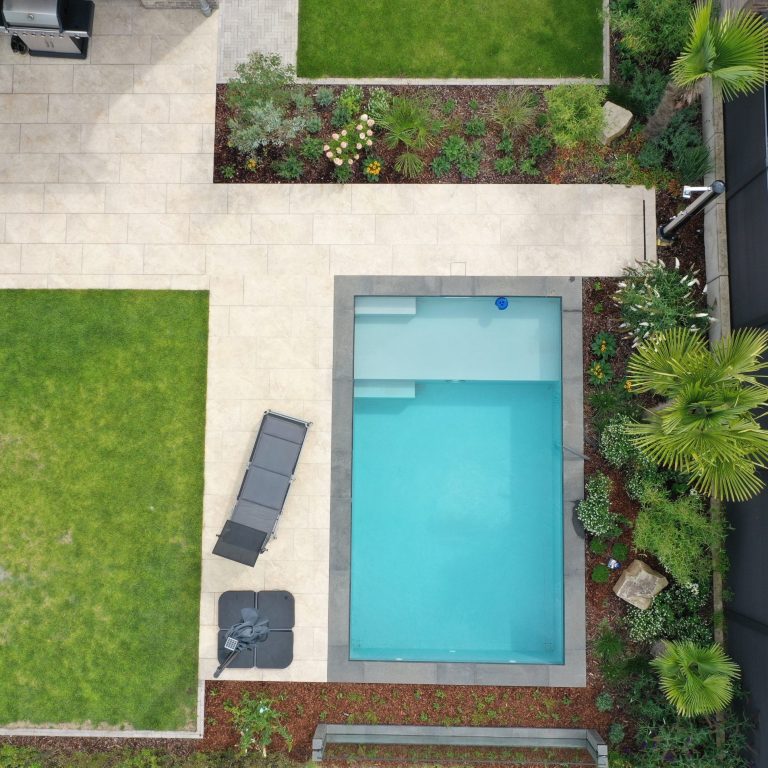 Gartenansicht mit Pool, Liege und gepflanzten Beeten.